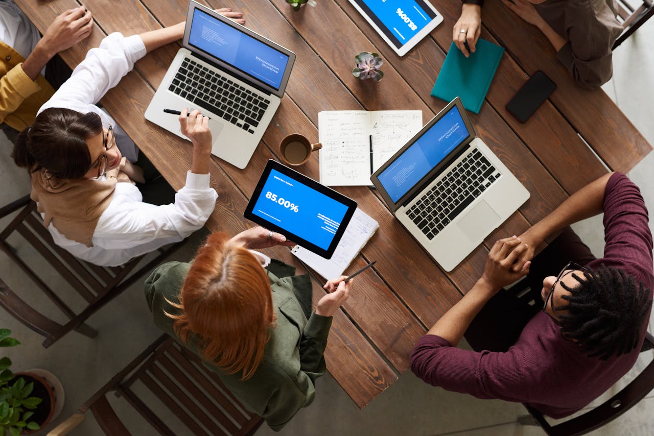 Services-01 Diverse team discussing business strategies with laptops and tablets at a wooden table.